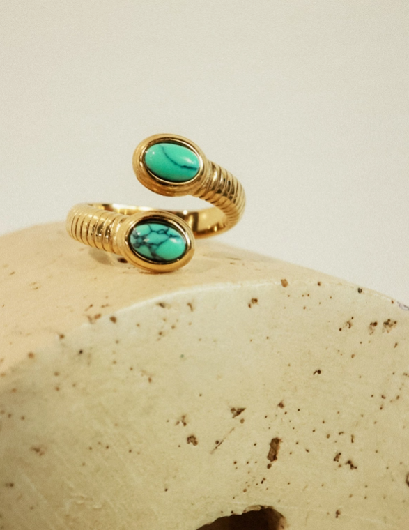 Gold ring with turquoise stones on a beige stone surface