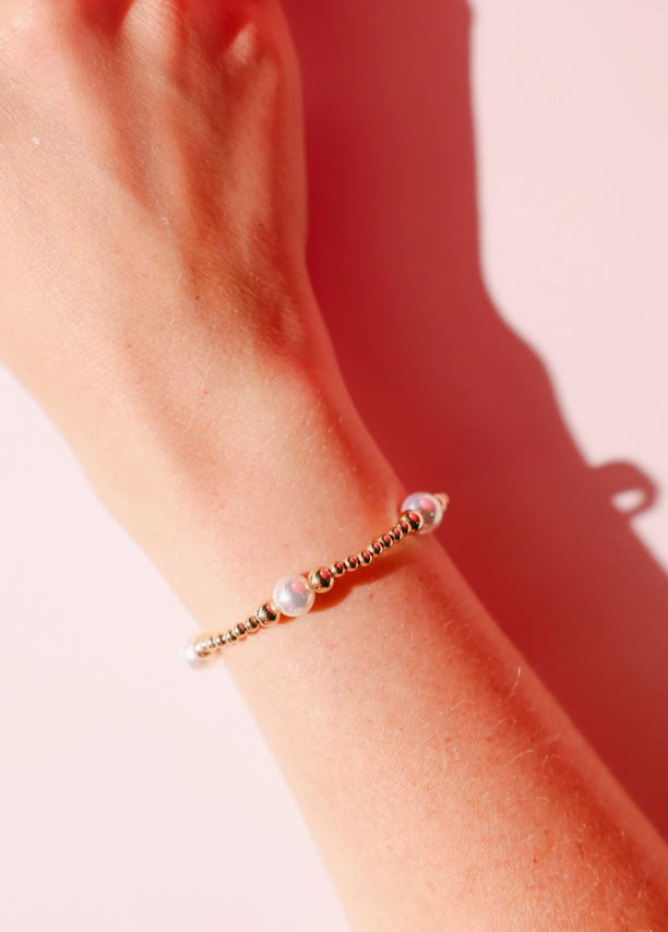 Close-up of a wrist wearing a beaded blondes bracelet on a pink background serena gold and pearl 