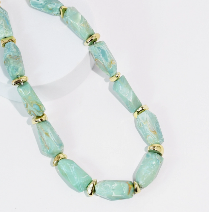Turquoise beaded necklace with gold accents on a white background