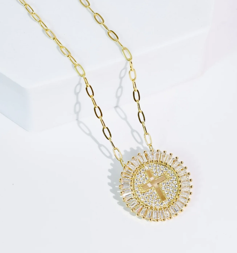 Gold necklace with a circular pendant featuring a cross on a light gray background