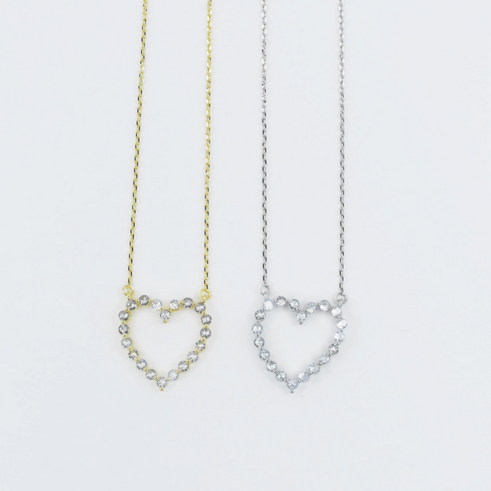 Two heart-shaped necklaces, one gold and one silver, on a light gray background.