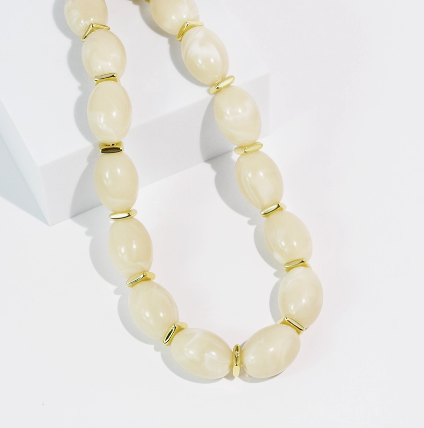 Beige beaded necklace with gold accents on a white background