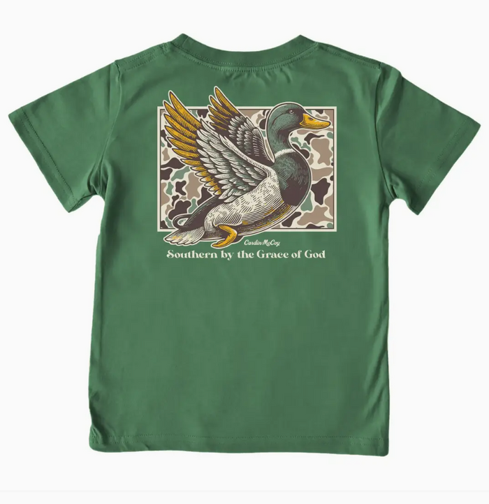 A green short-sleeve t-shirt shown flat against a white background, featuring a large graphic print of a flying mallard duck on a camouflage background with the text ' Southern by the Grace of God' printed below.