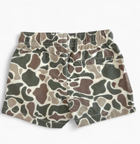 A pair of children's shorts featuring an all-over organic camouflage pattern in shades of olive green, brown, beige, and gray, displayed flat against a light off-white background.