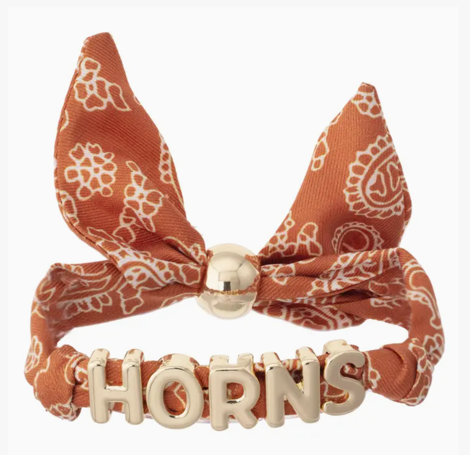 An orange and white paisley bandana bow headband with a gold-tone metal clasp and 'HORNS' lettering on the band, shown against a plain white background.