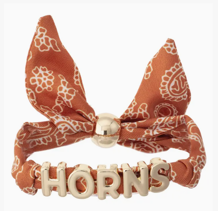 An orange and white paisley bandana bow headband with a gold-tone metal clasp and 'HORNS' lettering on the band, shown against a plain white background.
