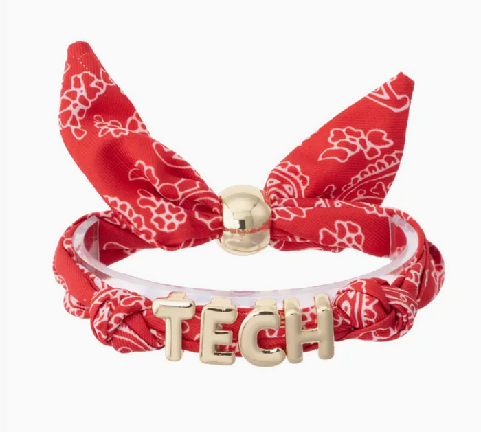 A red bandana-patterned bracelet featuring a bow, a clear acrylic band, and a gold-tone 'TECH' letter charm on a white background.
