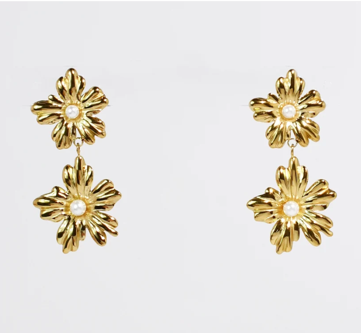 A pair of gold daisy drop earrings with textured petals and a small white pearl at the center, shown against a plain light gray background.