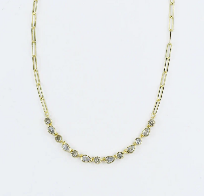 A gold paperclip chain necklace featuring a row of small teardrop-shaped clear gemstones in gold settings, displayed against a plain white background.
