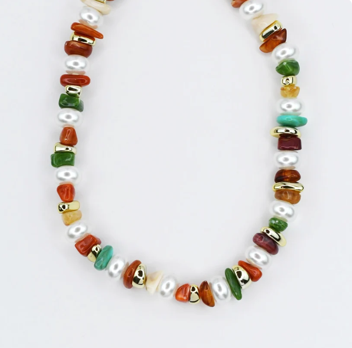 A beaded necklace featuring white freshwater pearls and polished stone chips in orange, green, red, and turquoise, accented with small gold spacer rings, displayed on a clean white background.