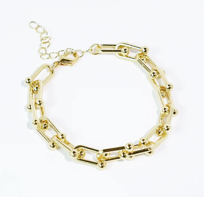 A gold chain link bracelet with alternating elongated paperclip-style links and small round bead accents, displayed on a clean white background.