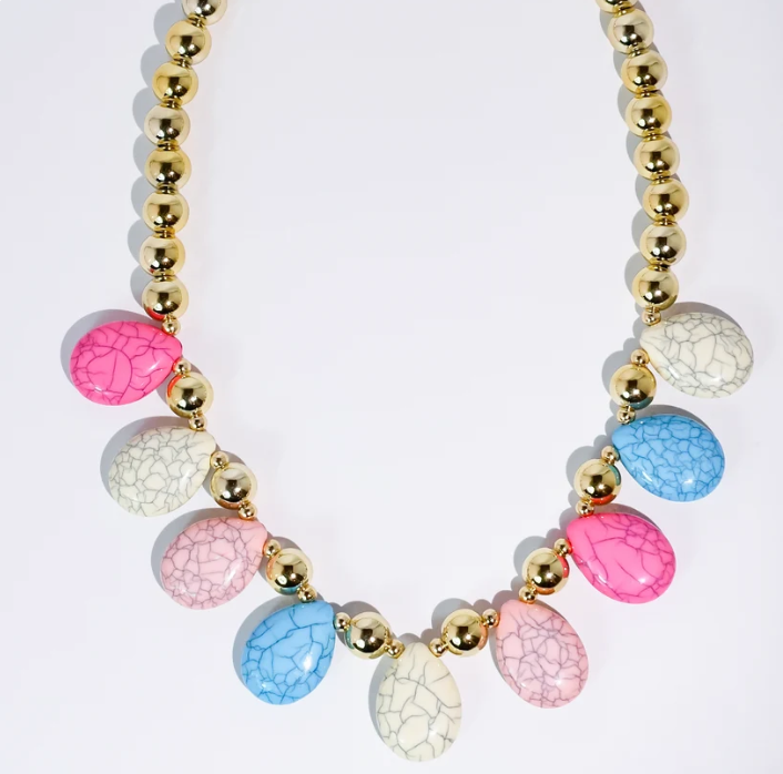 A statement necklace featuring a gold beaded chain and teardrop-shaped crackle enamel charms in pink, blue, and cream, arranged symmetrically on a white background.