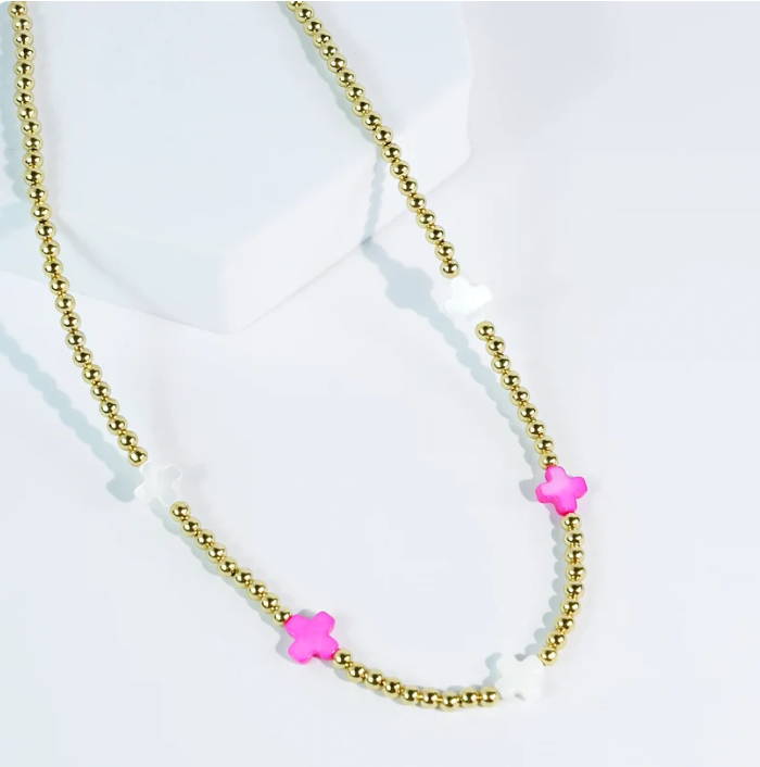 A gold beaded necklace with three pink flower charms and white translucent beads, displayed on a white geometric stand.