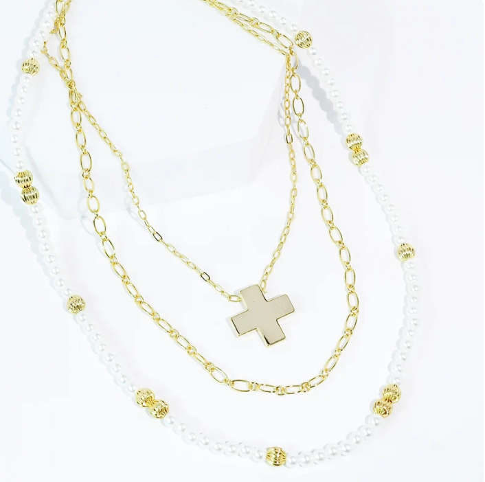 A layered necklace set featuring a gold cross pendant on a delicate gold chain, alongside a white pearl strand adorned with gold spacer beads.