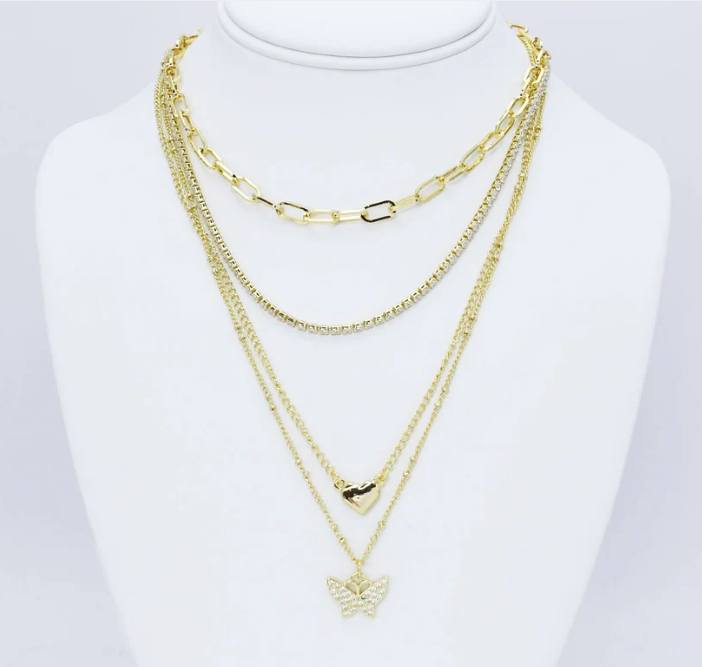 A gold multi-layered necklace set displayed on a white mannequin bust. The set includes a chunky paperclip chain, a fine curb chain, a delicate chain with a small heart pendant, and a longer chain with a butterfly pendant.