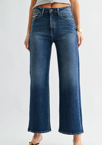 A model wearing a pair of dark blue wide-leg denim jeans, cropped from the waist down, shown against a plain light gray studio background.