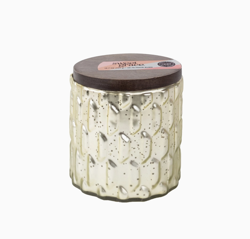 A textured glass jar candle with a dark wood lid, featuring a cream-colored body with subtle speckles and a pink and gold label on top. sweet grace 