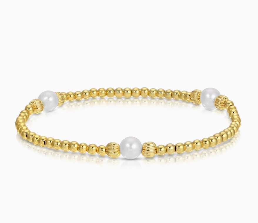 A gold beaded bracelet with three white pearl-like beads, displayed on a clean white background with a soft reflection.