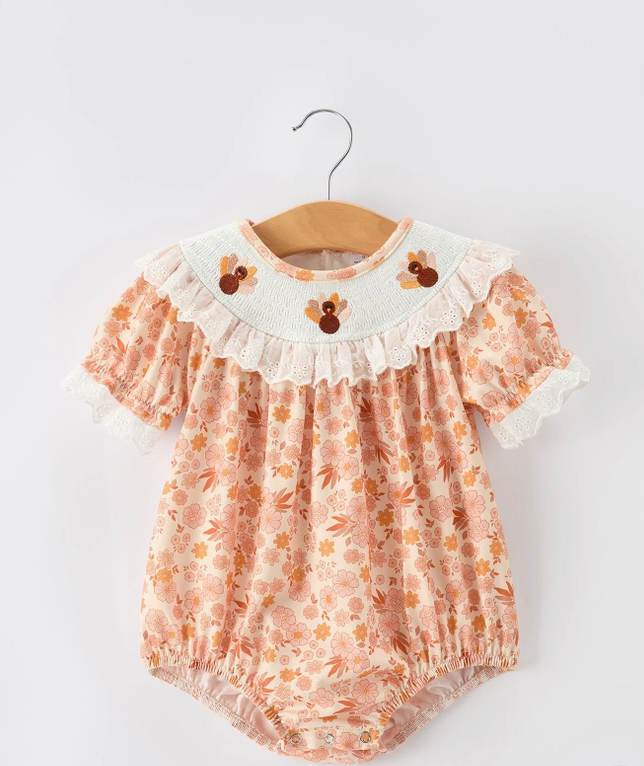 A baby girl's short-sleeve romper in a peach and orange floral print, featuring a white ruffled collar with embroidered cartoon birds and lace trim, hanging on a wooden hanger against a light gray background.