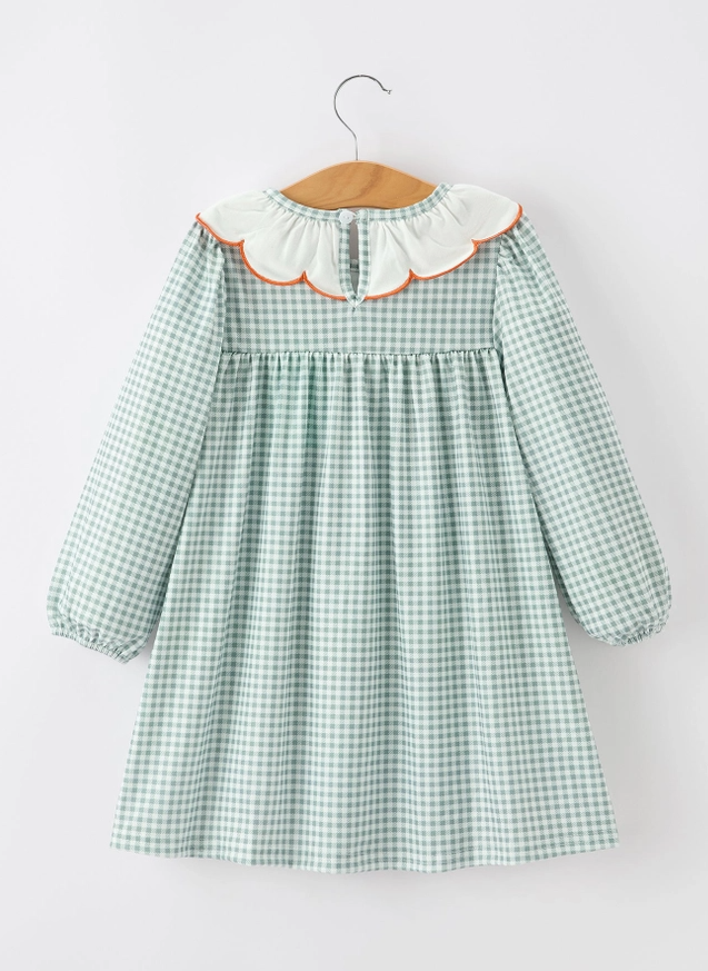A light green and white gingham long-sleeve dress for a toddler, featuring a white ruffled collar with orange trim, hanging on a wooden hanger against a plain white background.