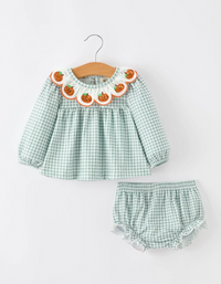 A two-piece baby girl's outfit set featuring a long-sleeve smocked blouse and matching bloomers in a light green and white gingham pattern. The blouse has a decorative ruffled collar decorated with embroidered orange pumpkins 
