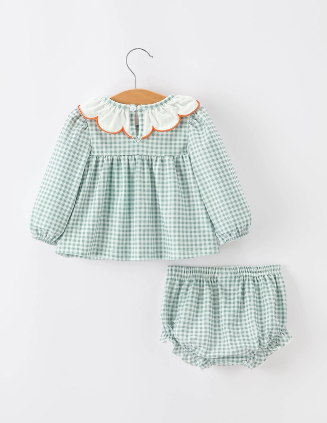 A two-piece baby girl's outfit set featuring a long-sleeve green and white gingham dress with a white ruffled collar trimmed in orange, paired with matching green and white gingham bloomers, displayed on a wooden hanger against a light gray background.