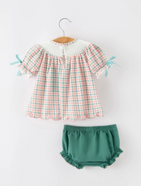 A toddler girl's two-piece outfit set featuring a short-sleeve top with a pink, green, and white gingham plaid pattern, a white collar, and light blue ribbon bows on the sleeves, paired with matching green ruffled bloomers, displayed on a wooden hanger against a white background.