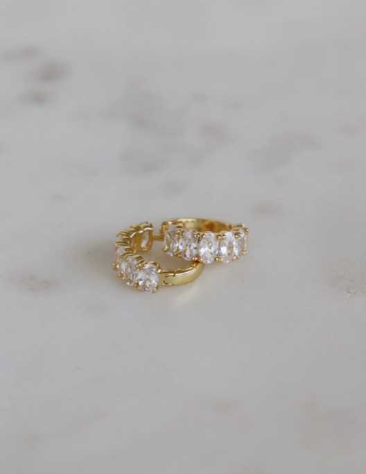 Gold hoop earrings with clear stones on a light gray marble background