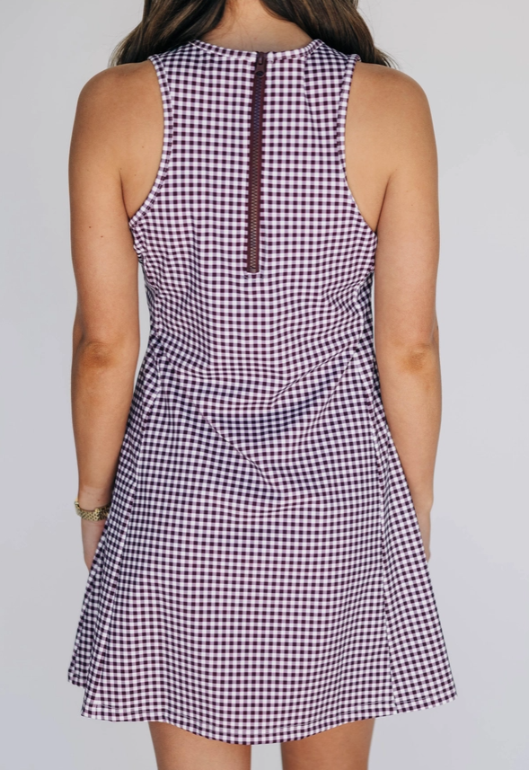 Back view of a person wearing a sleeveless checkered dress on a plain background