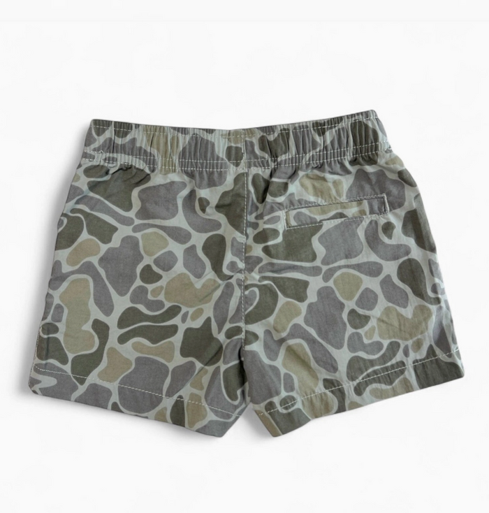 A pair of children's shorts featuring an abstract organic pattern in shades of olive green, gray, and beige, with an elastic waistband and side pockets, shown against a plain white background.