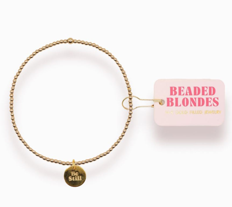 Gold beaded bracelet with 'Be Still' charm on a white background, featuring the brand 'Beaded Blondes'.
