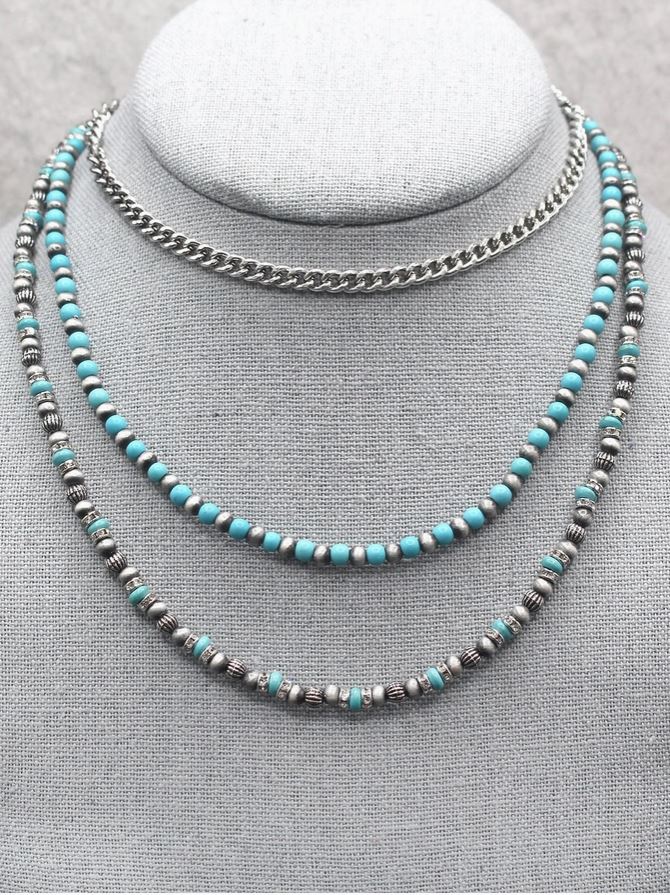 Two necklaces with turquoise beads and silver chain on a gray stand.