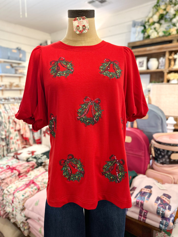red short sleeve top with red and green sequin wreath design for christmas and holiday 
puff sleeves inside store setting 