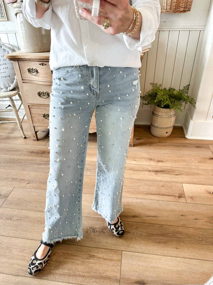 Person wearing light blue jeans with pearls and gemstones indoors on a wooden floor.