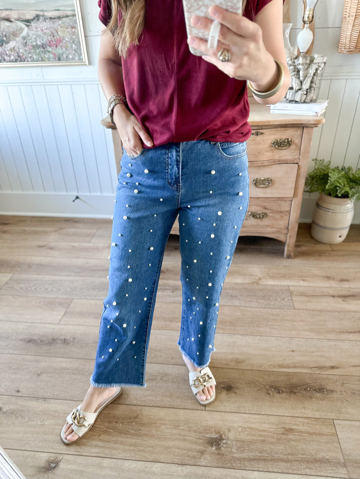 Person wearing blue jeans with white pearls in a room with wooden flooring and furniture. mud pie bullock pearl jeans 
