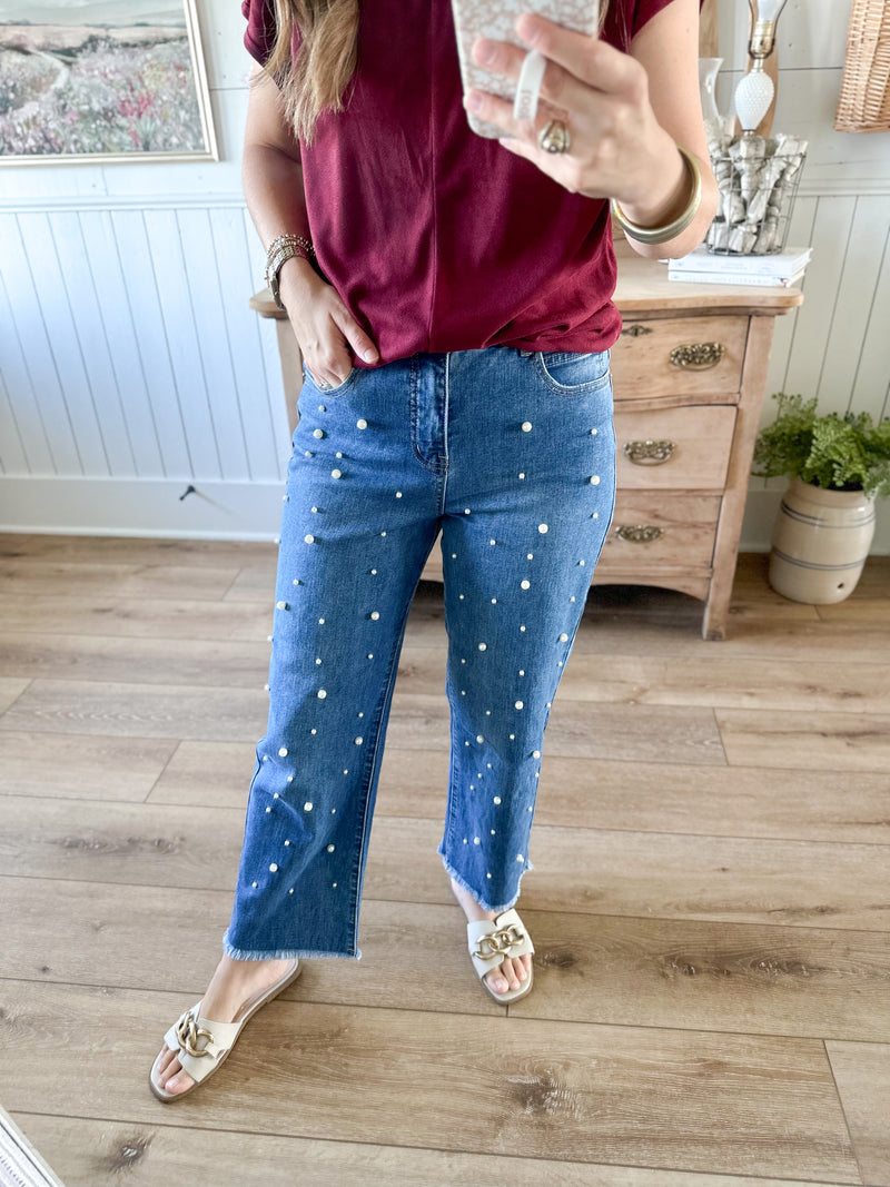 Person wearing blue jeans with white pearls in a room with wooden flooring and furniture. mud pie bullock pearl jeans 