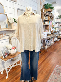 Mannequin wearing a beige blouse and blue jeans in a store setting with wooden floors and shelves.