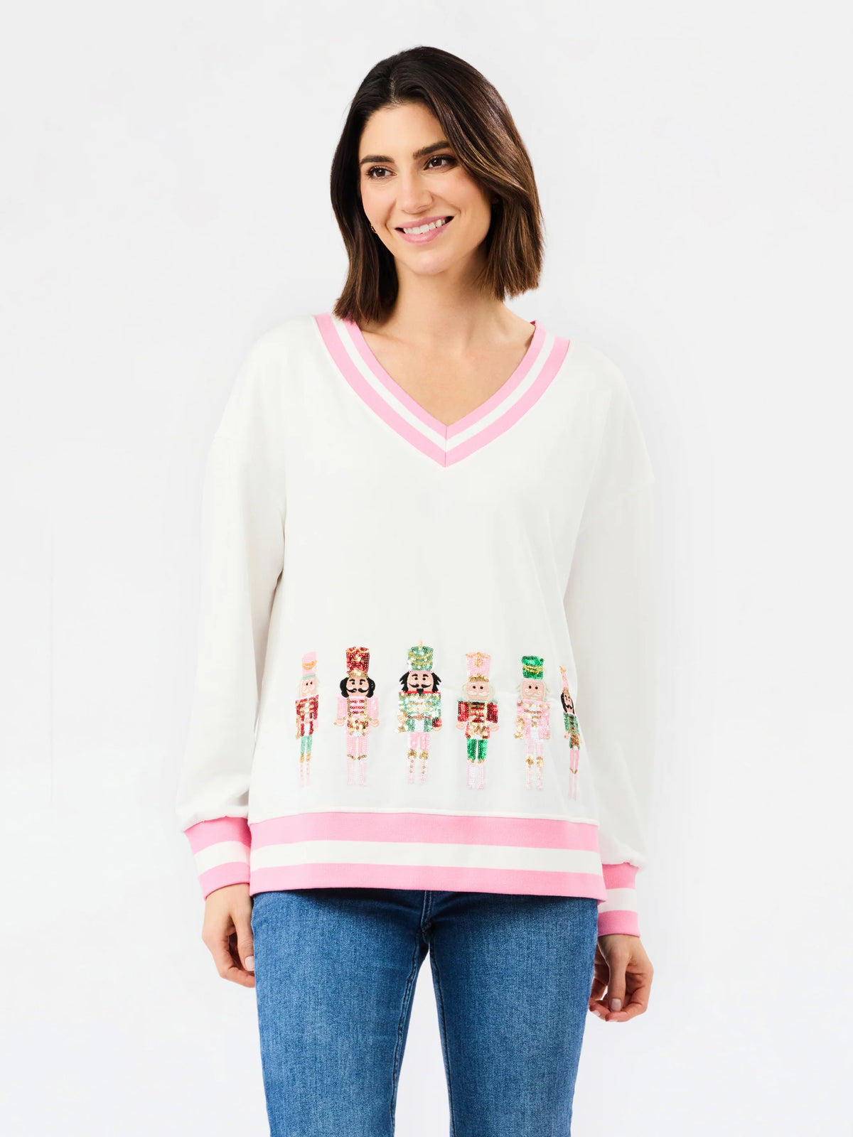 white sequin nutcracker holiday sweater v neck with pink and white band along hem of sweater on white background 
